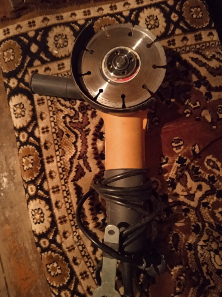 A rugged corded angle grinder sitting on a sheet of raw steel, symbolizing how to use AI to choose the best tool for a DIY BBQ grill project. Use AI to Choose the Best Angle Grinder
